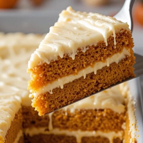 A warm slice of pumpkin gooey butter cake with creamy pumpkin cream cheese topping, garnished with a sprinkle of cinnamon and powdered sugar.